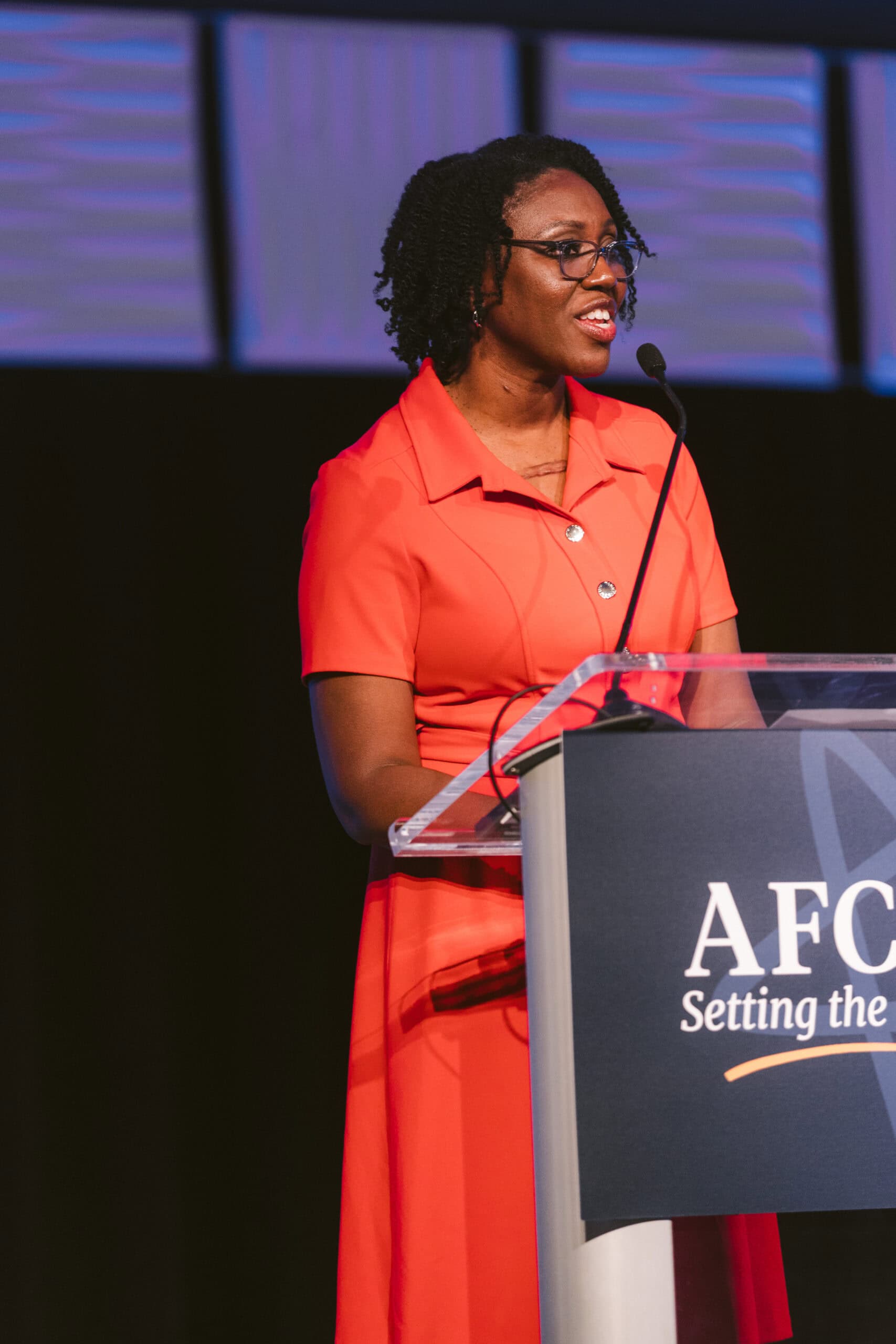 Brandy standing behind a microphone on a stage in a red dress